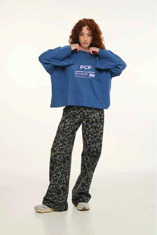 Person wearing a blue sweatshirt with text and patterned pants on a white background