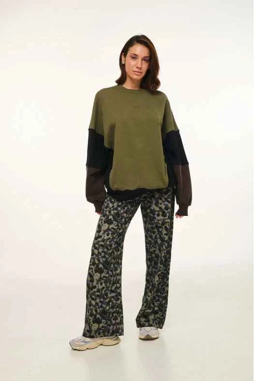 Person wearing a green and black sweater with patterned pants on a white background