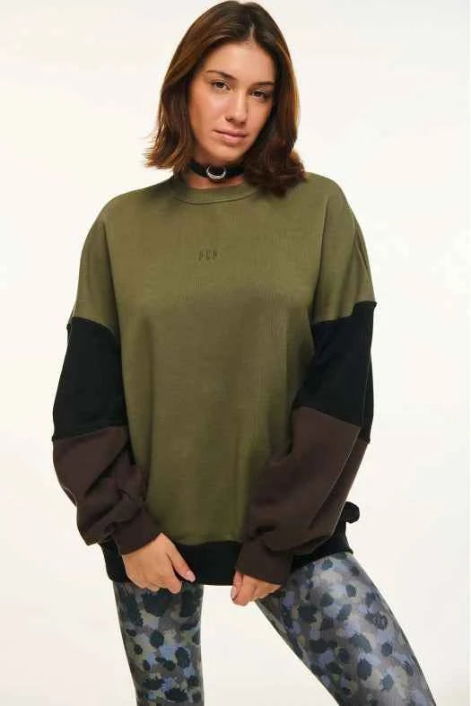 Person wearing a green and brown sweater with camouflage pants on a white background