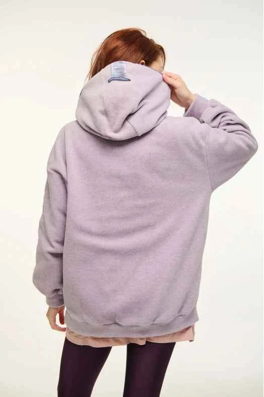 Person wearing a light purple hoodie with a small logo on the back, standing against a plain background.