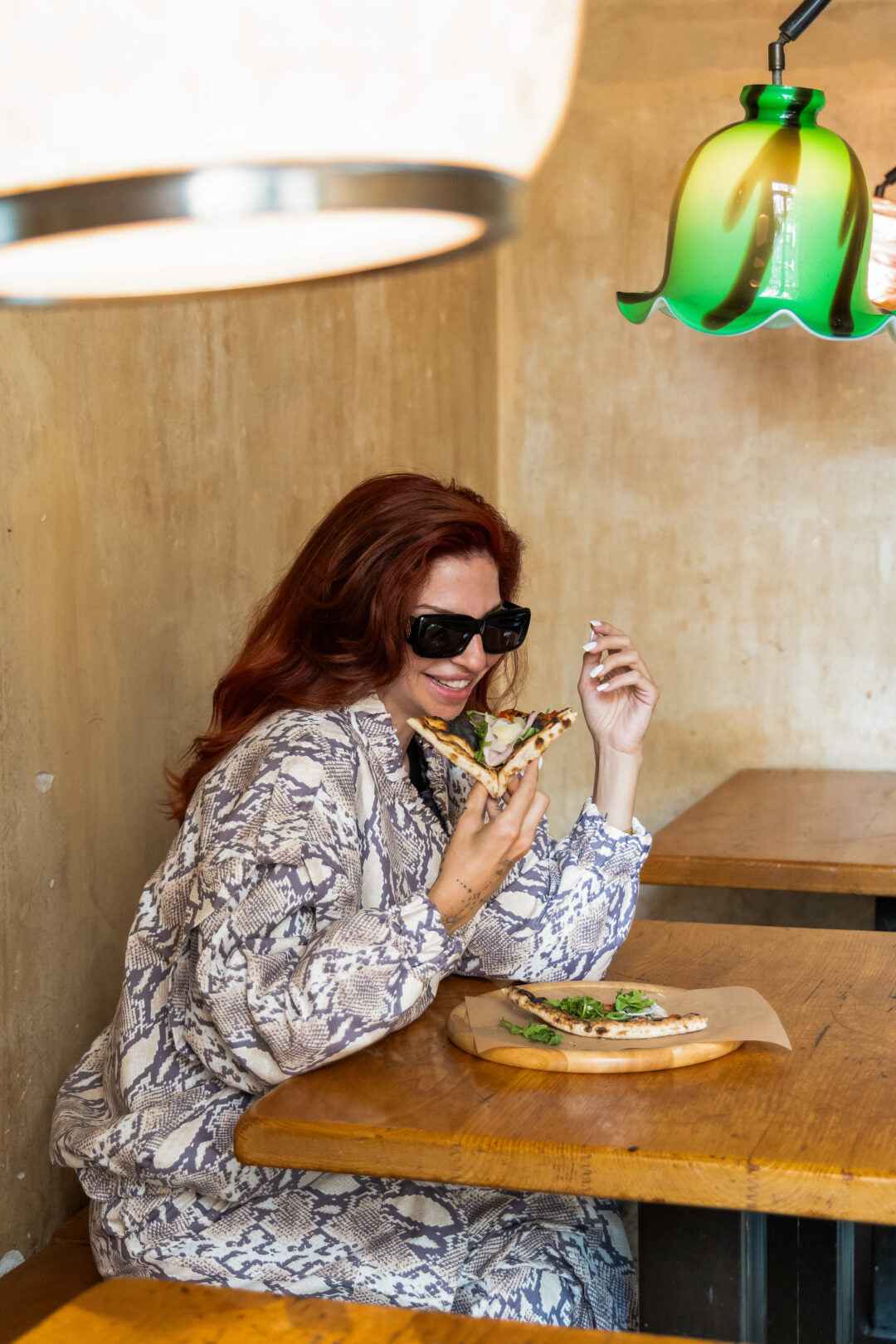 Woman in snakeskin print outfit eating pizza.