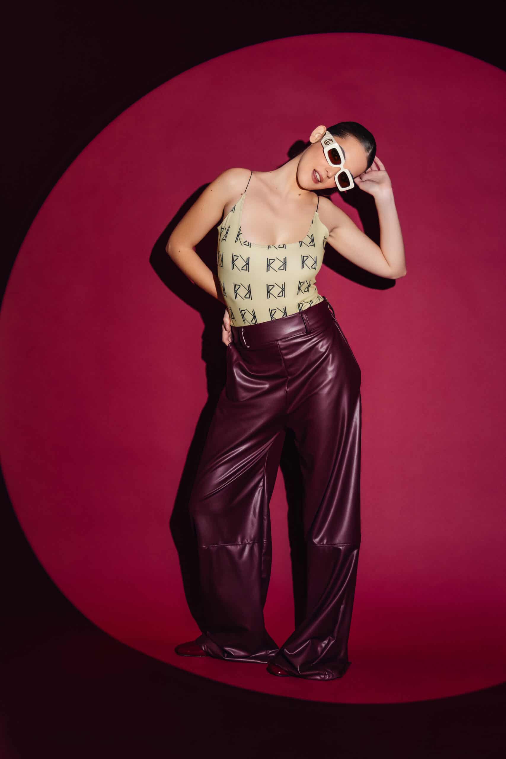 Person wearing a patterned top and shiny purple pants against a pink background