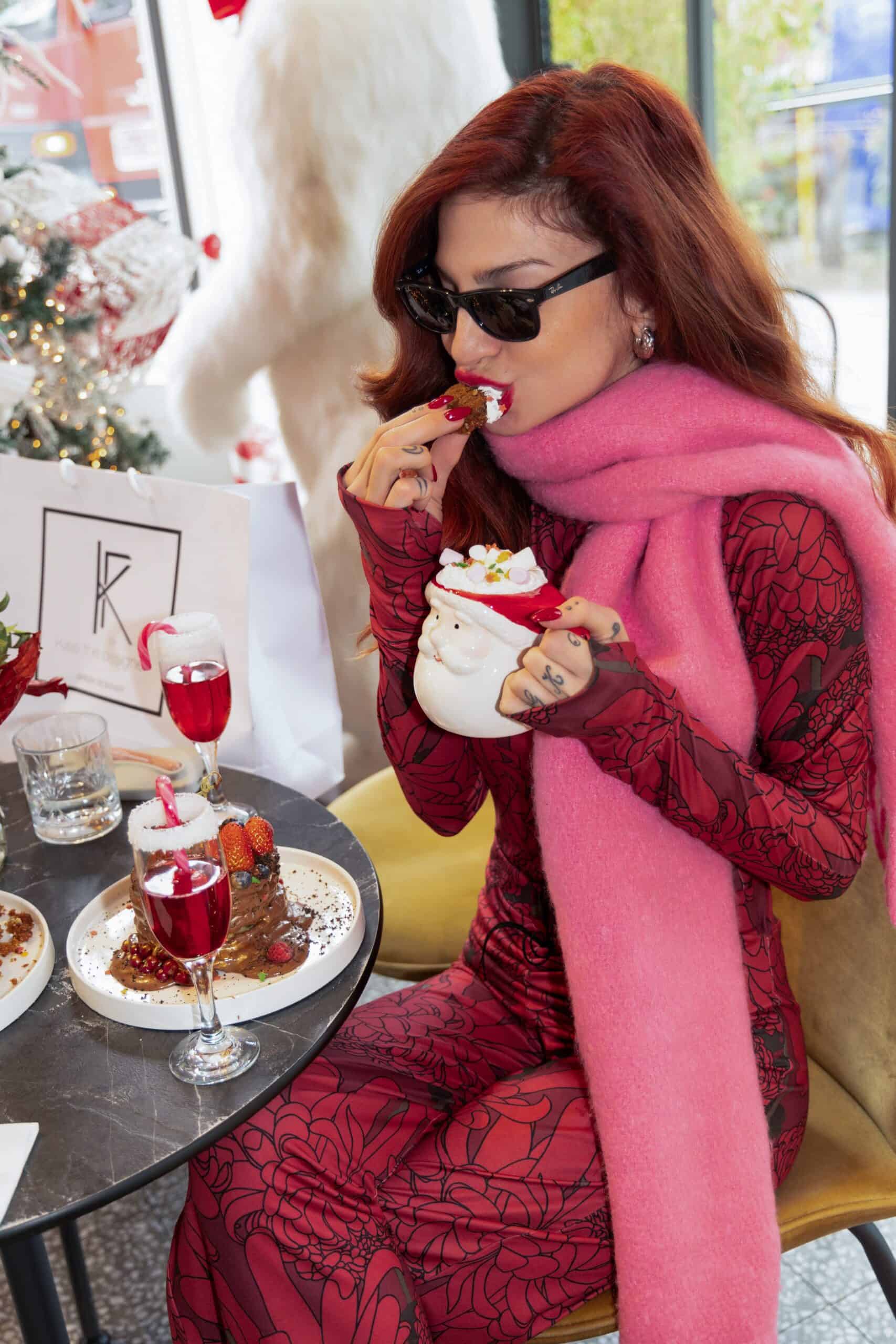 Woman in red patterned dress and pink scarf eating dessert in a festive setting