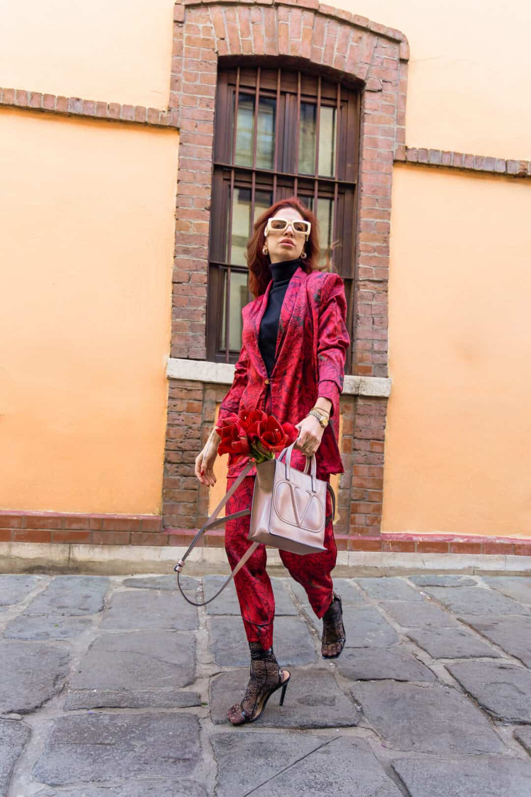Woman in a red outfit holding flowers against a brick wall.