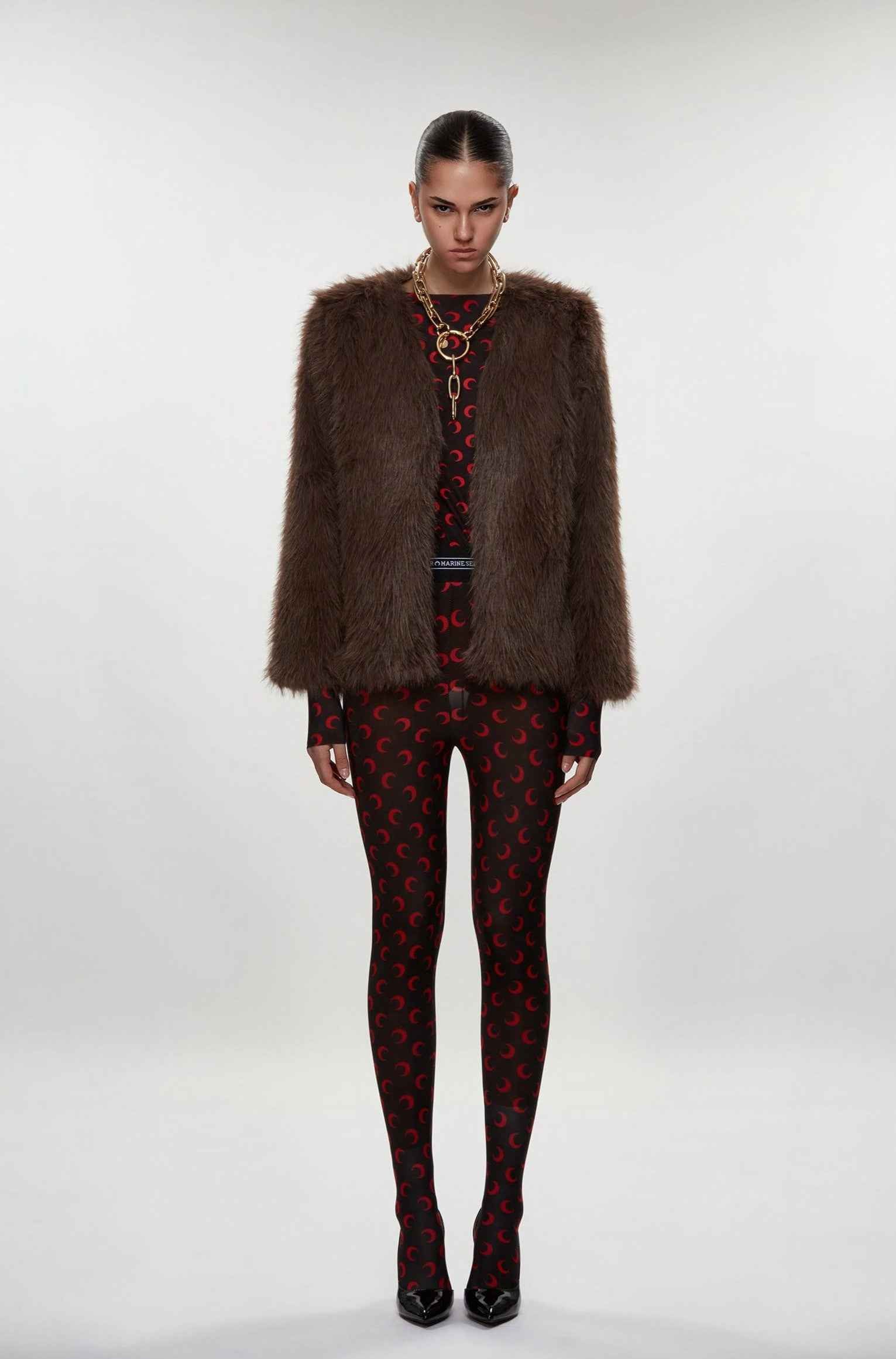 Model wearing a brown fur coat, patterned dress, and tights on a white background