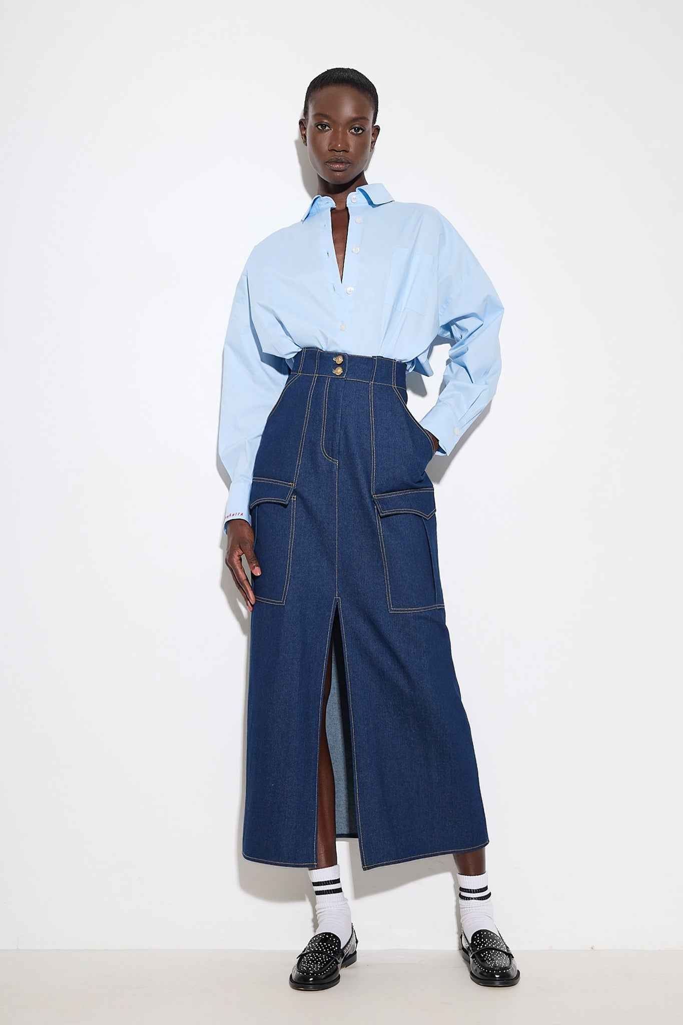 Person wearing a light blue shirt and blue denim jumpsuit on a white background