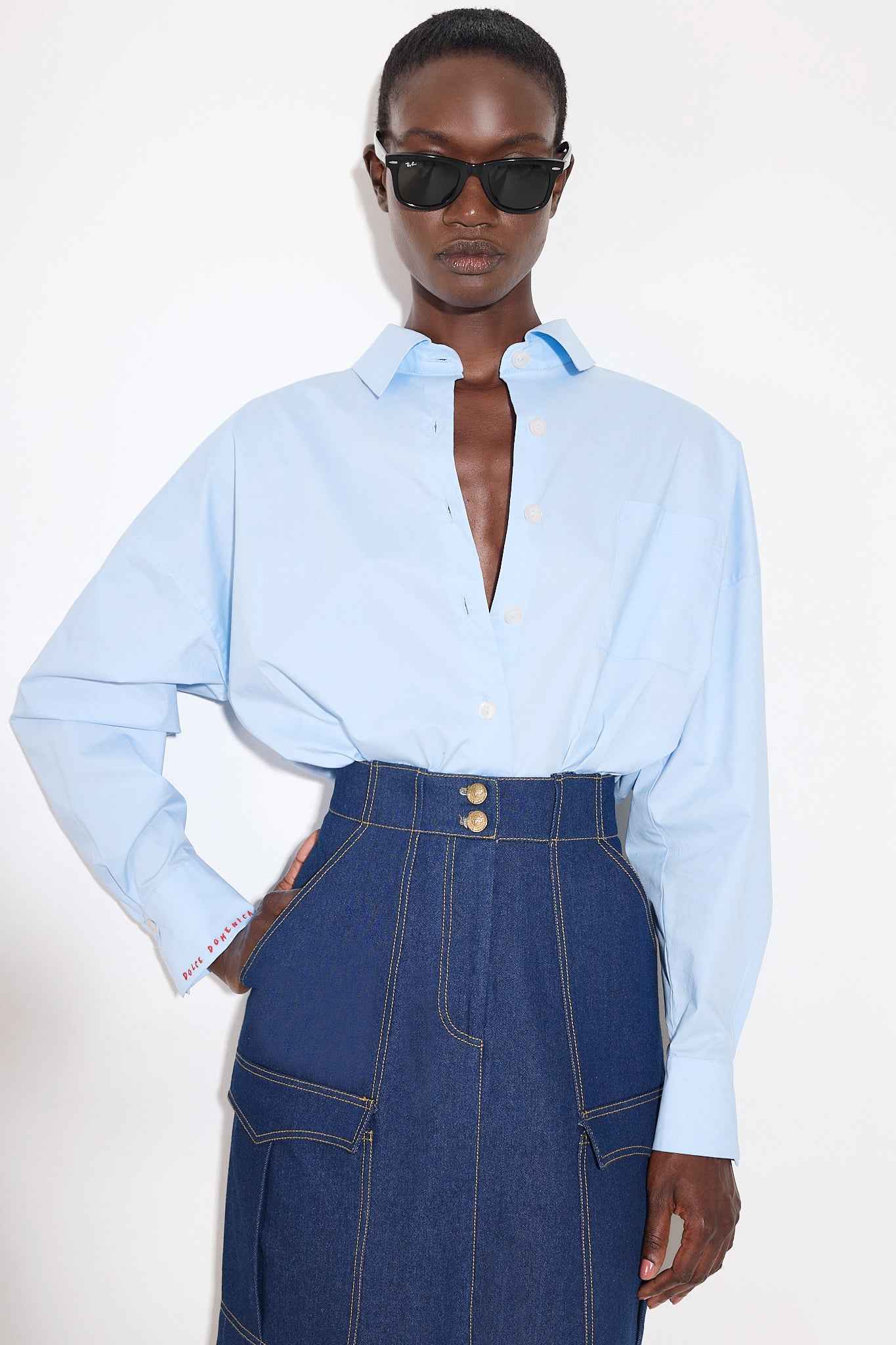 Person wearing a light blue shirt and denim skirt on a white background
