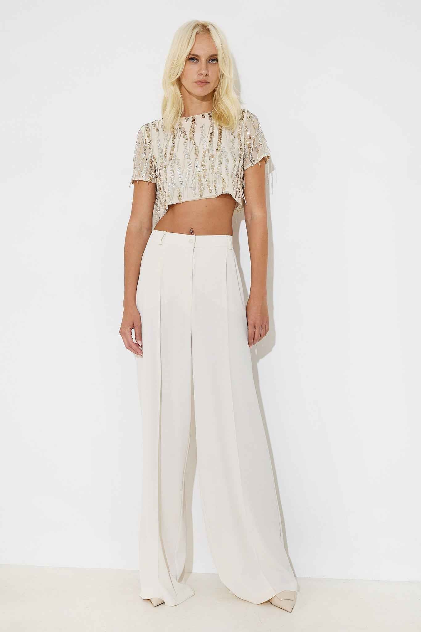 A woman wearing a white beaded crop top and high-waisted white palazzo pants.