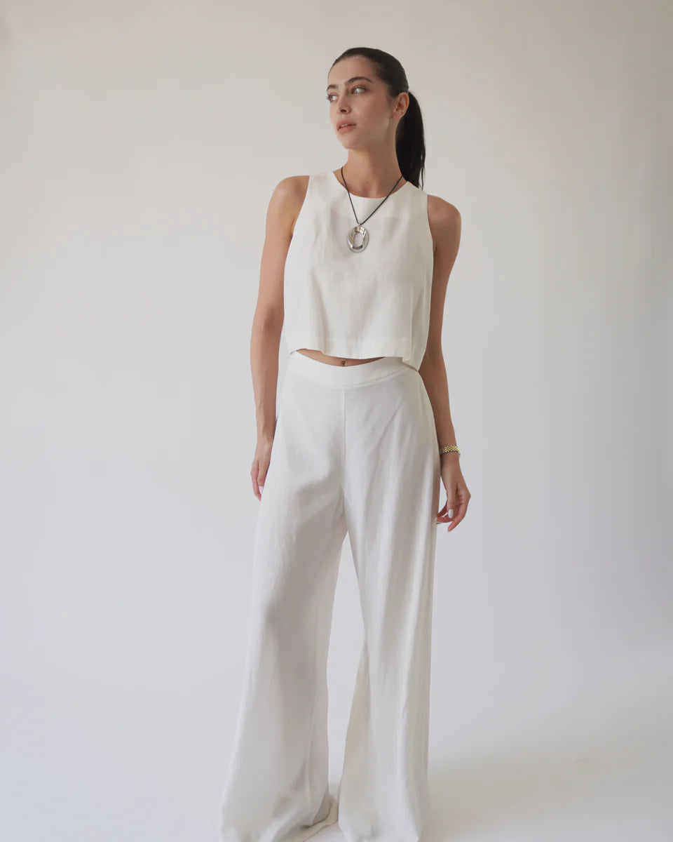 Woman wearing a white sleeveless top and wide-leg pants against a plain background