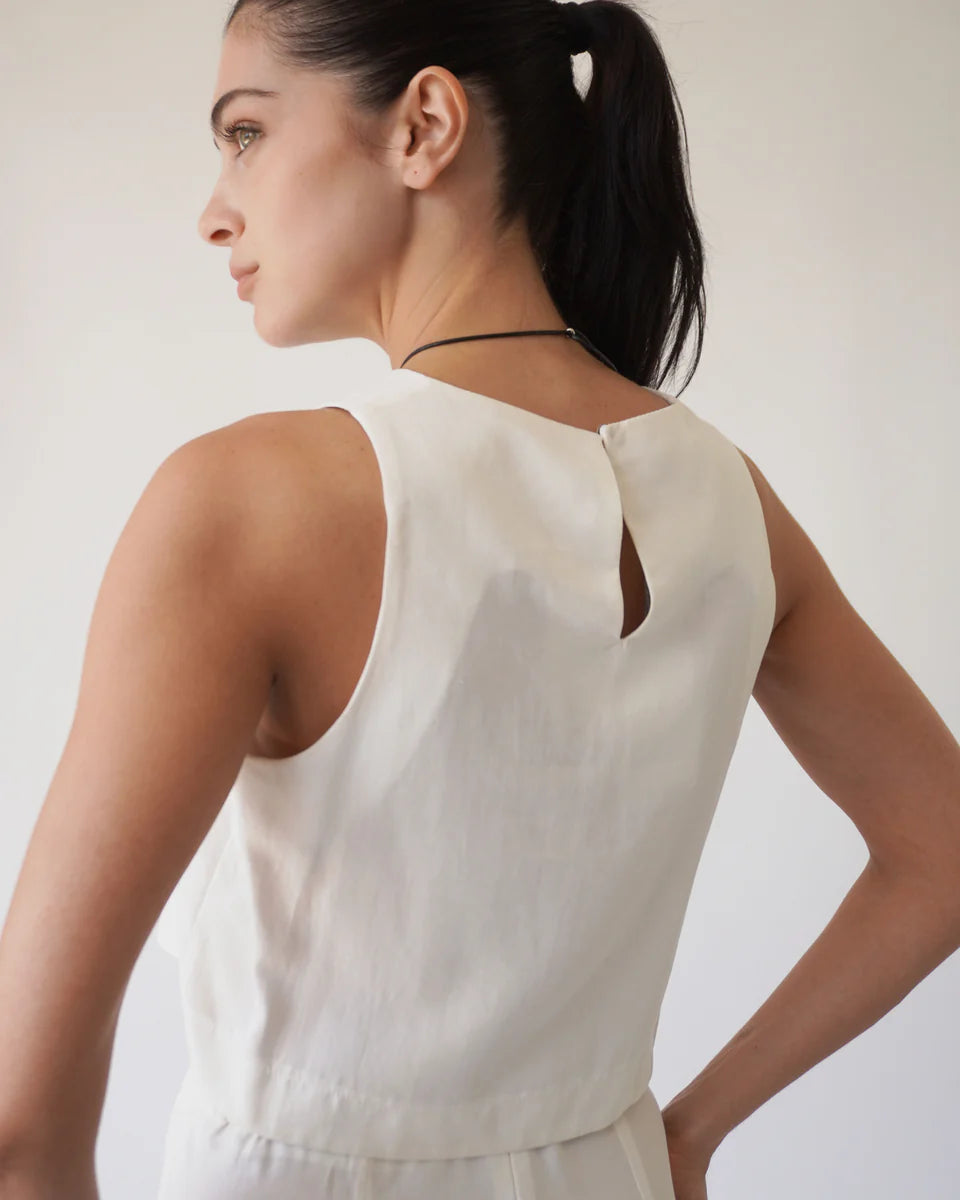 Woman wearing a white sleeveless top against a plain background