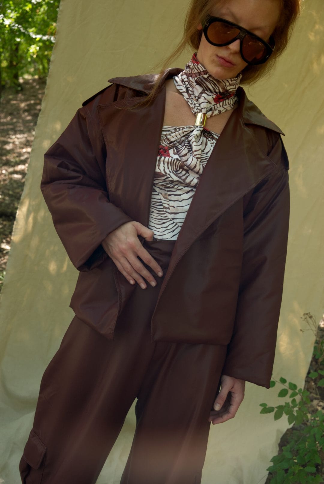 Person wearing a brown coat and sunglasses outdoors with a neutral background