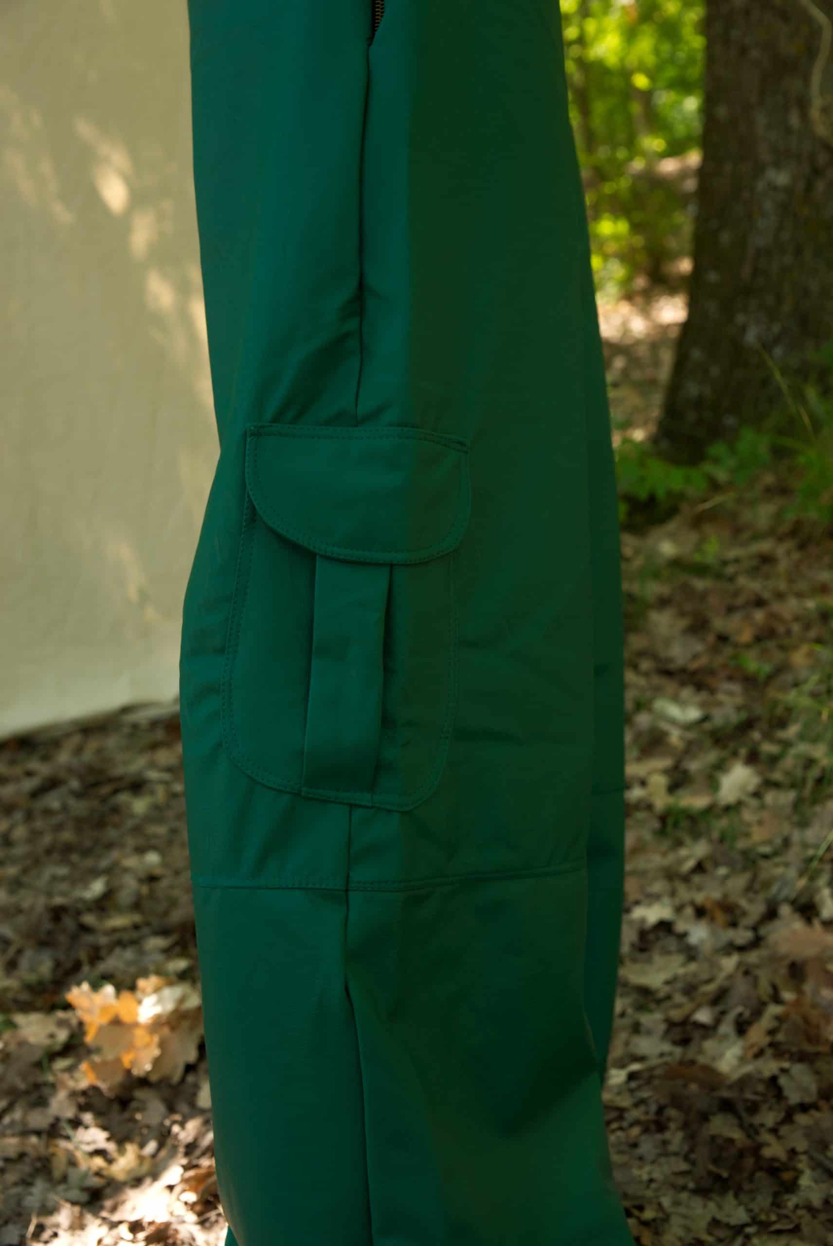 Green raincoat with a belt standing outdoors on a leafy ground.