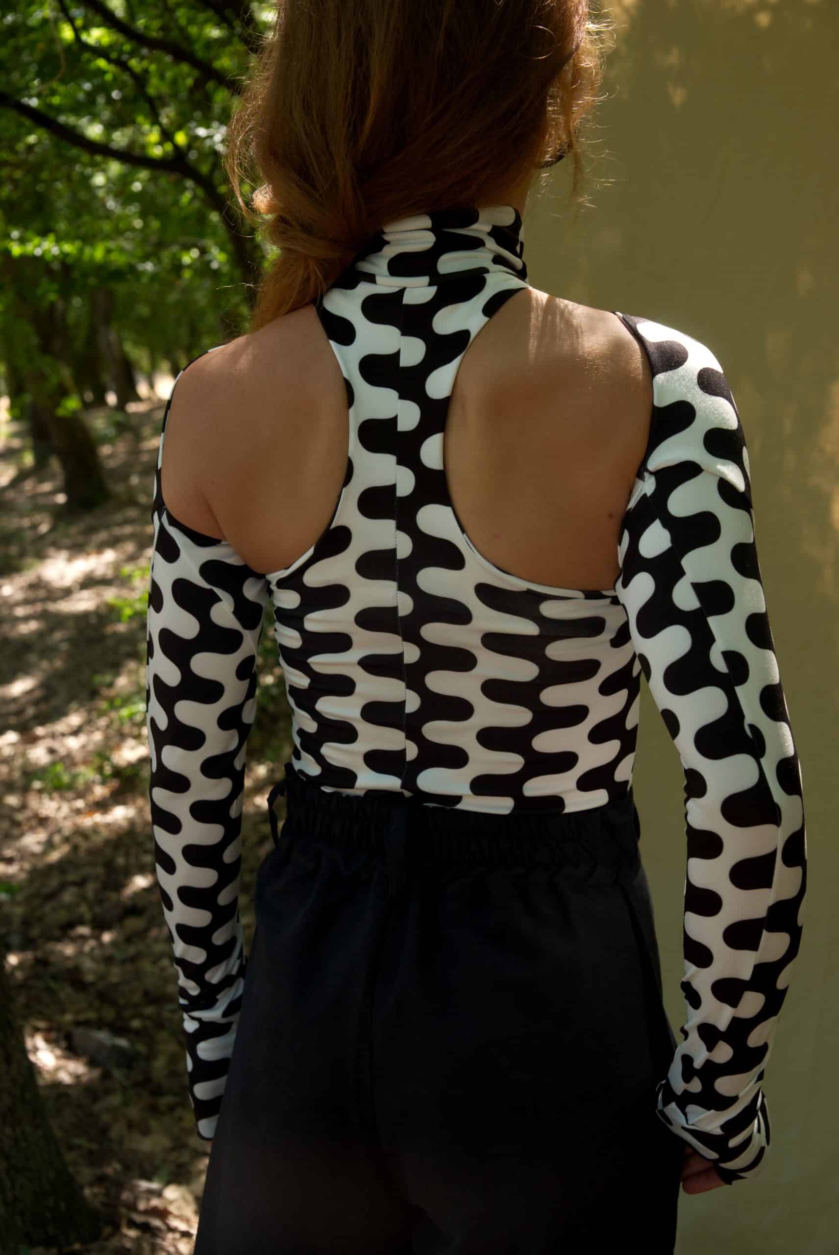 Person wearing a black and white patterned top with open back, standing outdoors.