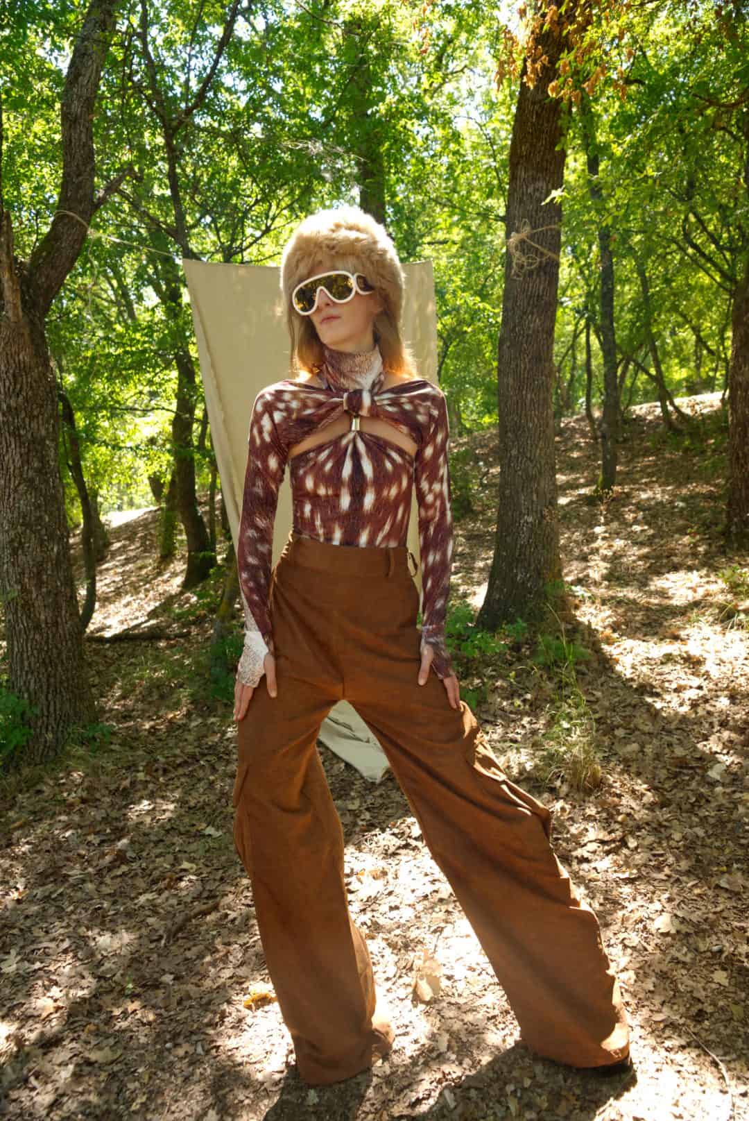Person in a forest wearing a patterned top and brown pants with sunglasses.