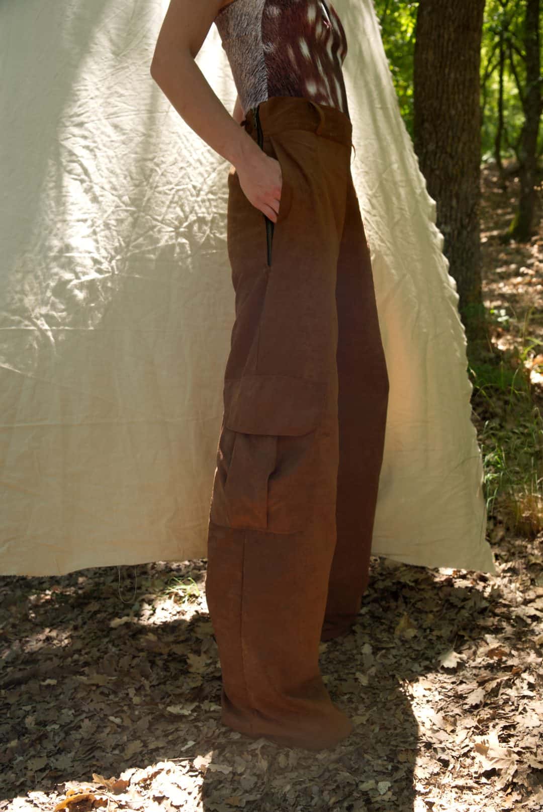 Person wearing brown cargo pants standing in front of a white tent in a forest setting