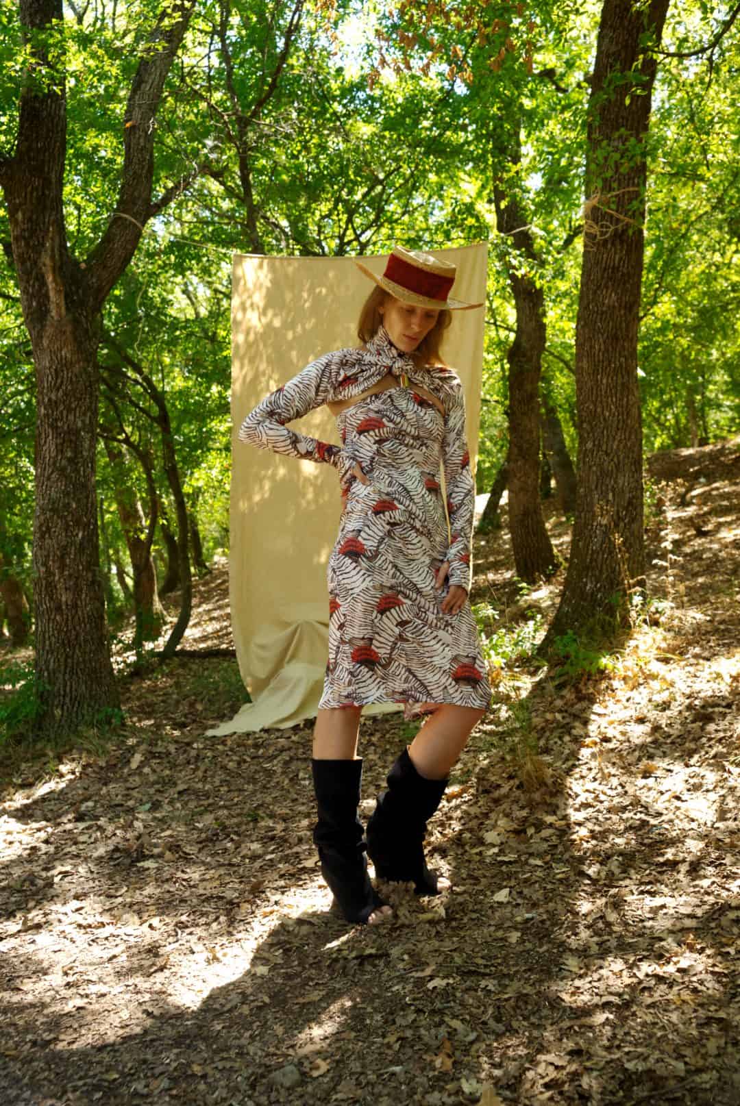 Woman in a patterned dress and hat standing in a forest
