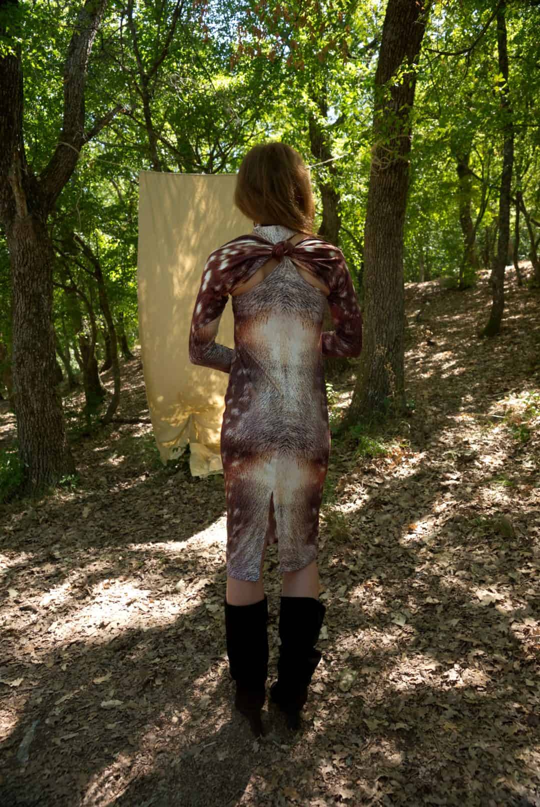 Person standing in a forest wearing a patterned dress and black boots.
