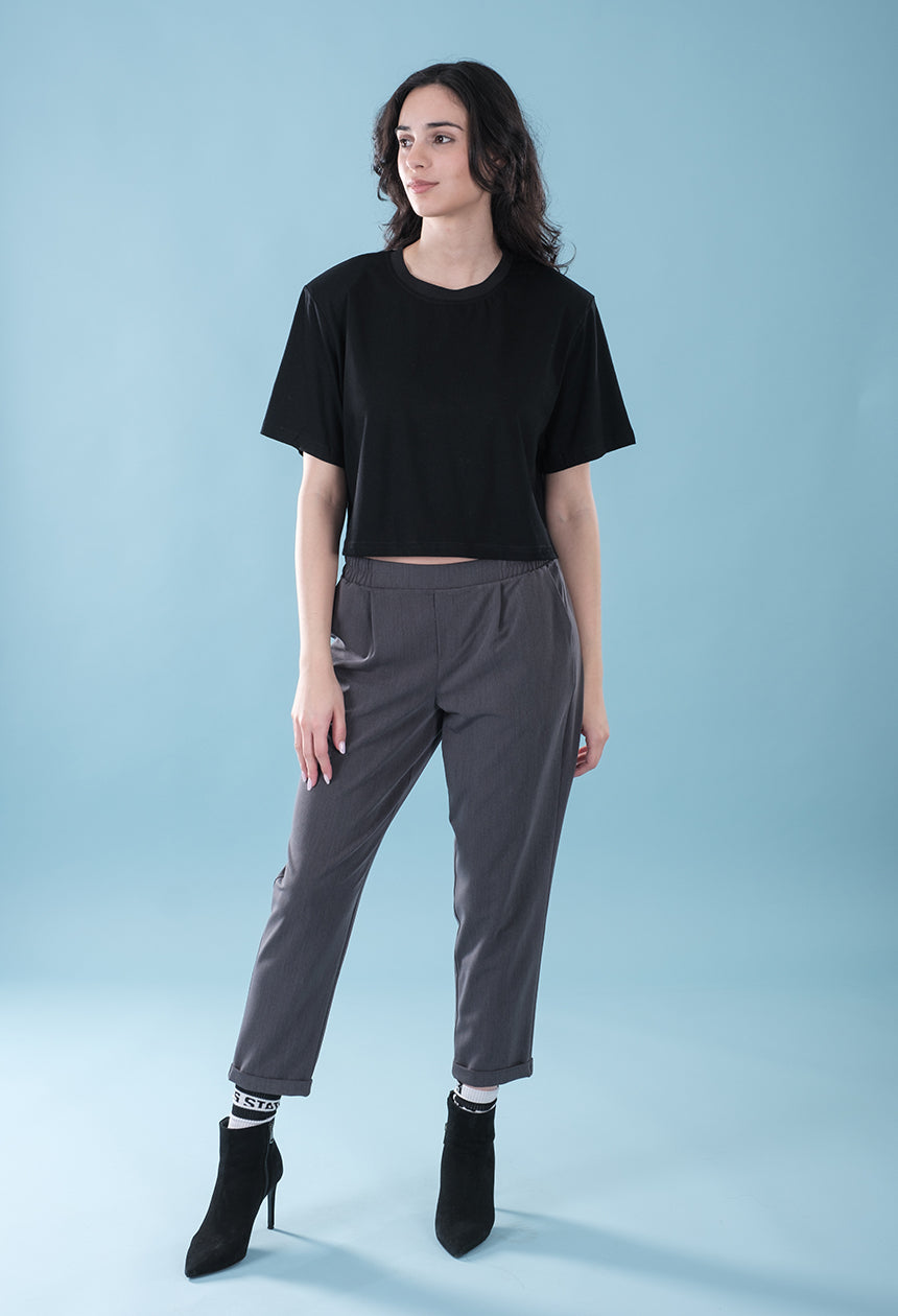 Woman wearing a black t-shirt and gray pants against a light blue background