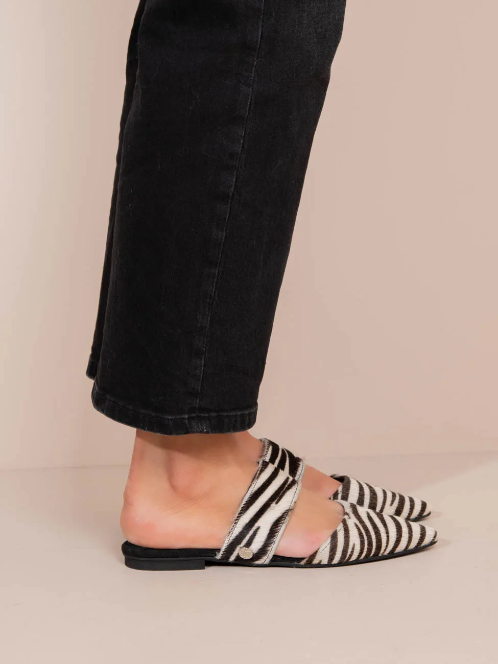 Person wearing zebra print slip-on shoes with black pants on a beige background