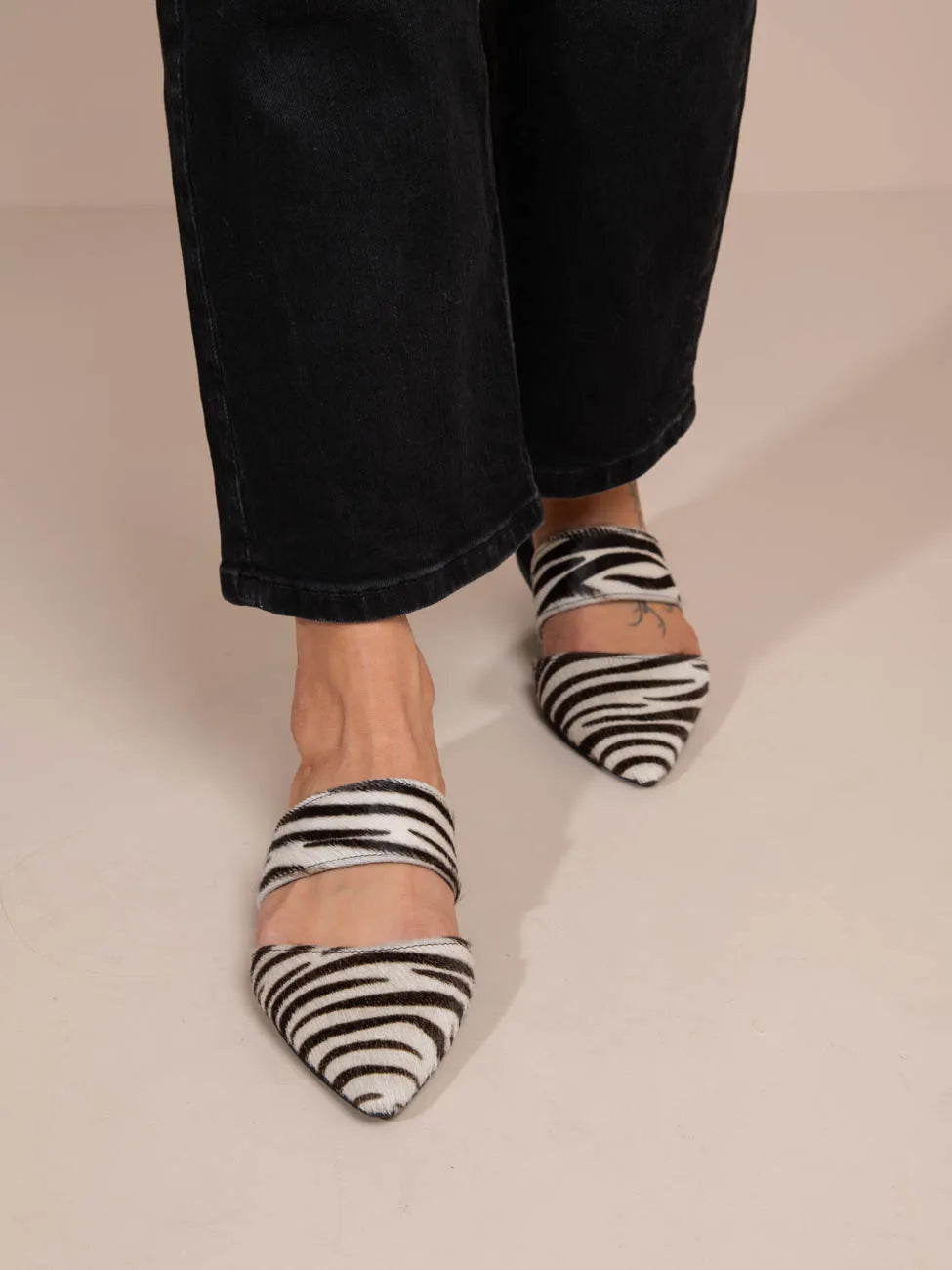 Zebra-striped pointed-toe shoes worn with black pants on a neutral background