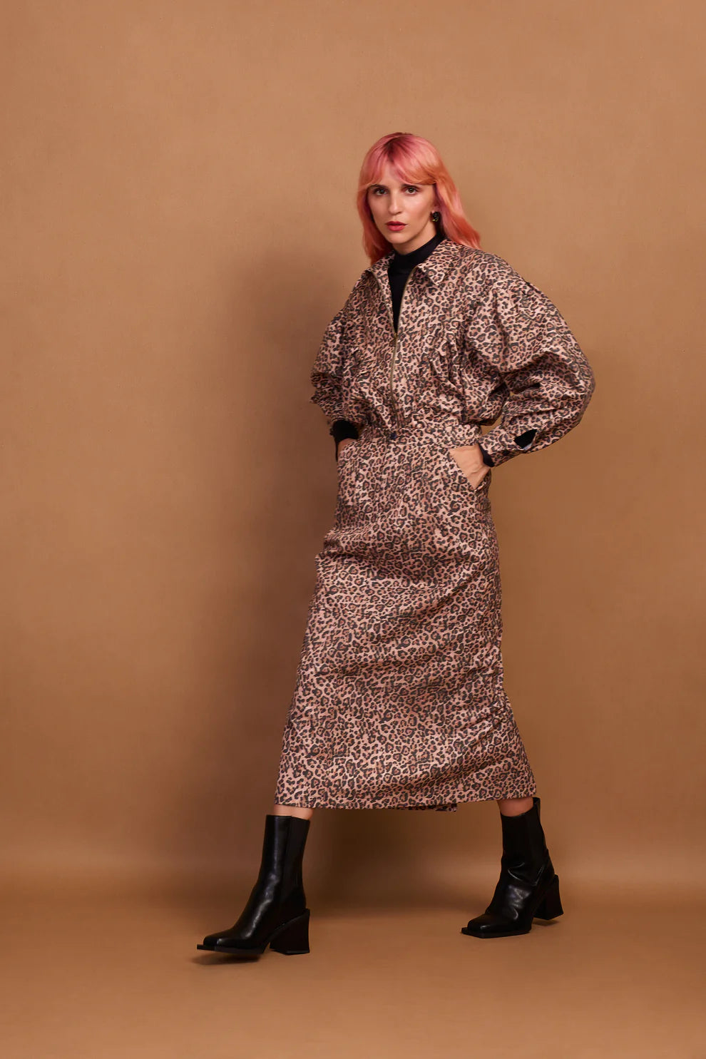 A model wearing a brown animal print zip jacket and standing against a plain background.