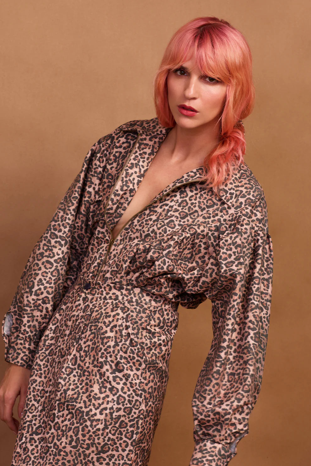 A model wearing a brown animal print zip jacket and standing against a plain background.