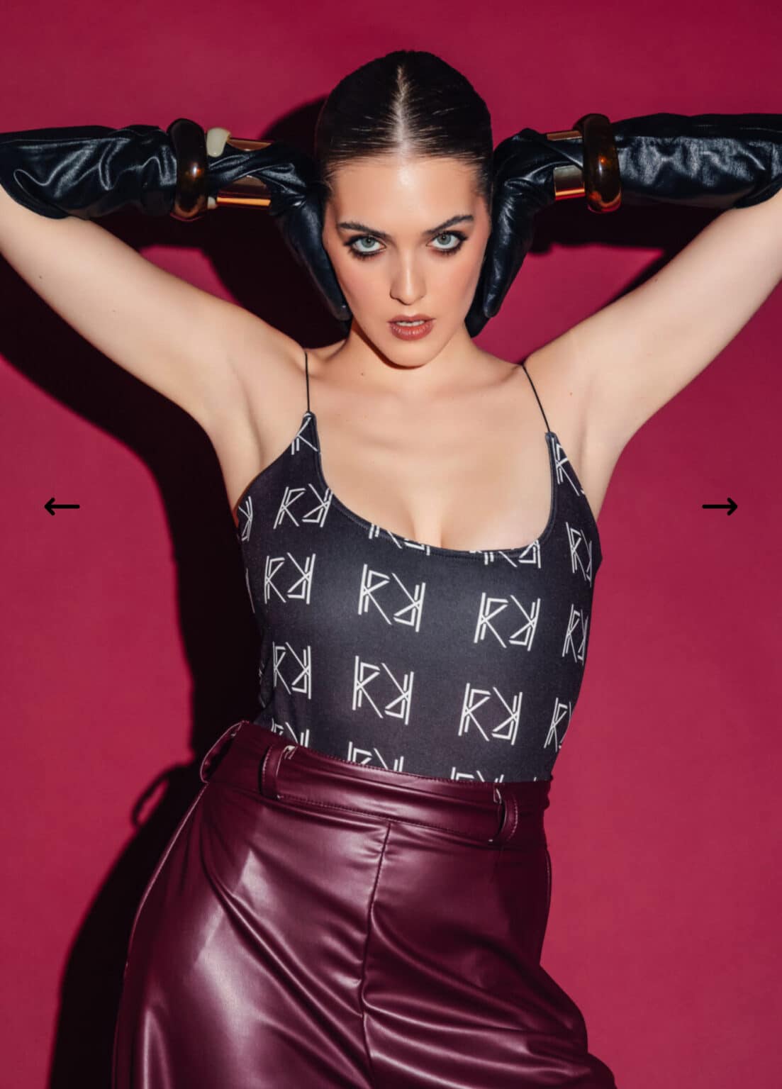 Woman wearing a black top with white logo and maroon pants against a pink background