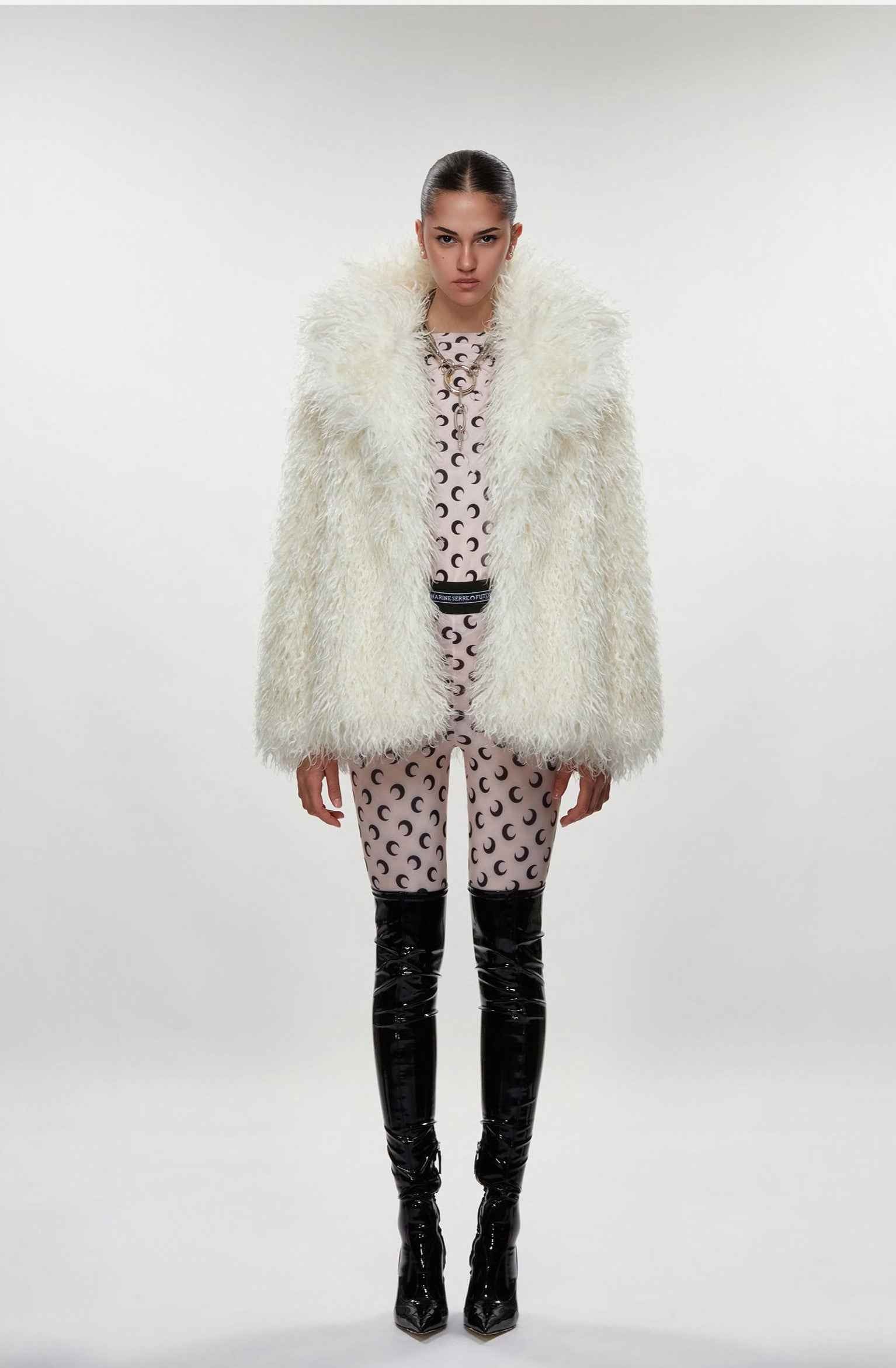 Model wearing a white fluffy coat, patterned dress, and black boots on a white background