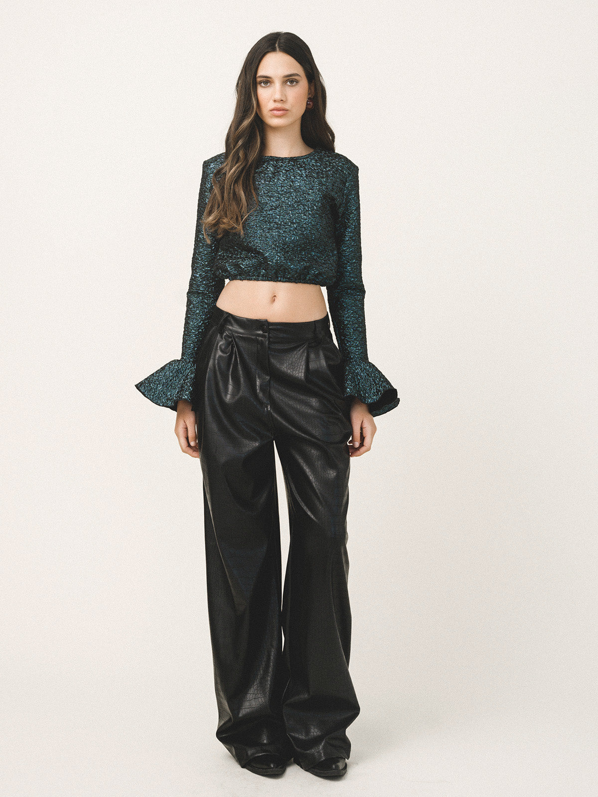 Woman wearing a blue sequin top and black satin pants on a white background