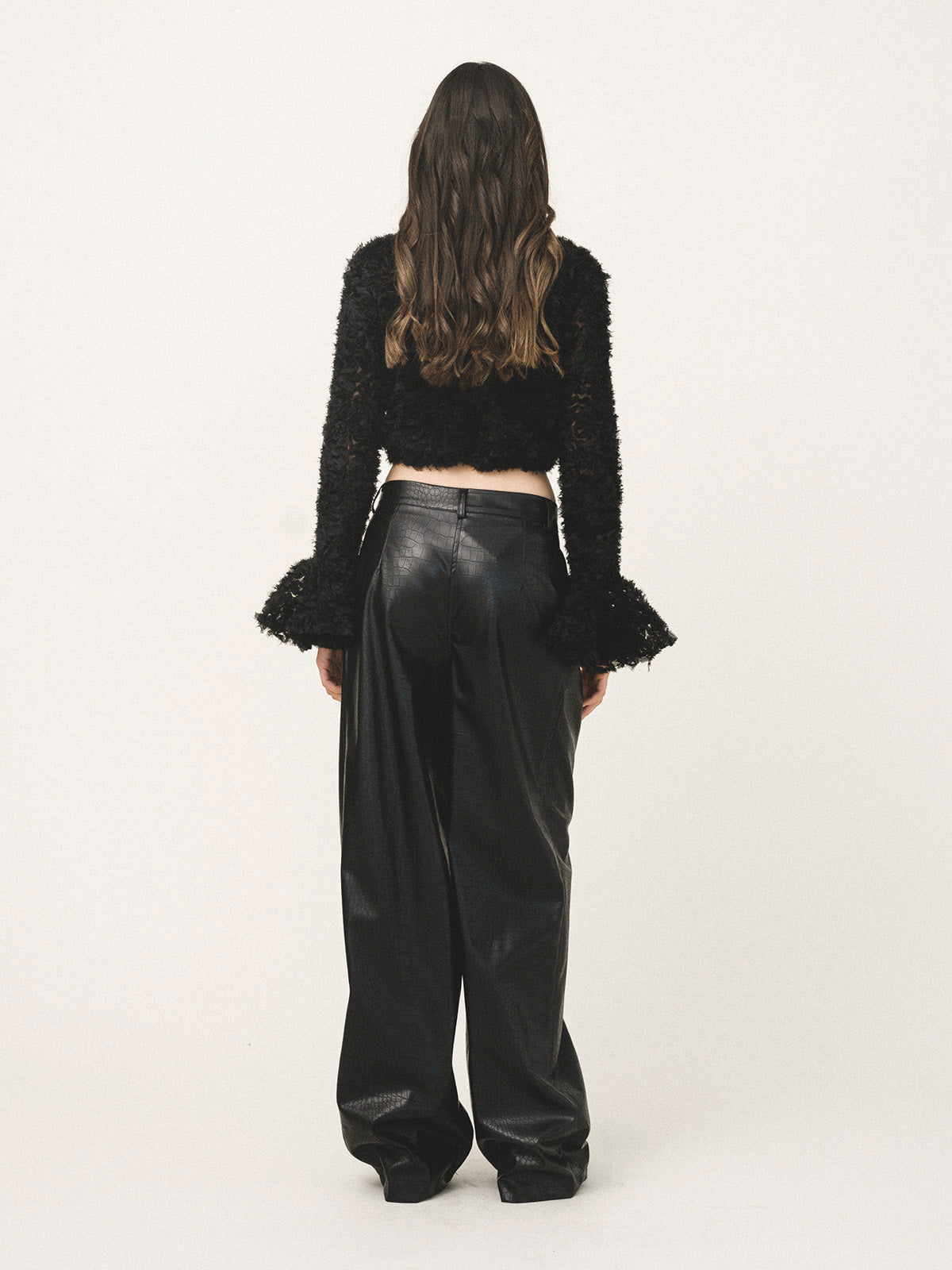 Person wearing a black textured top and leather pants on a white background
