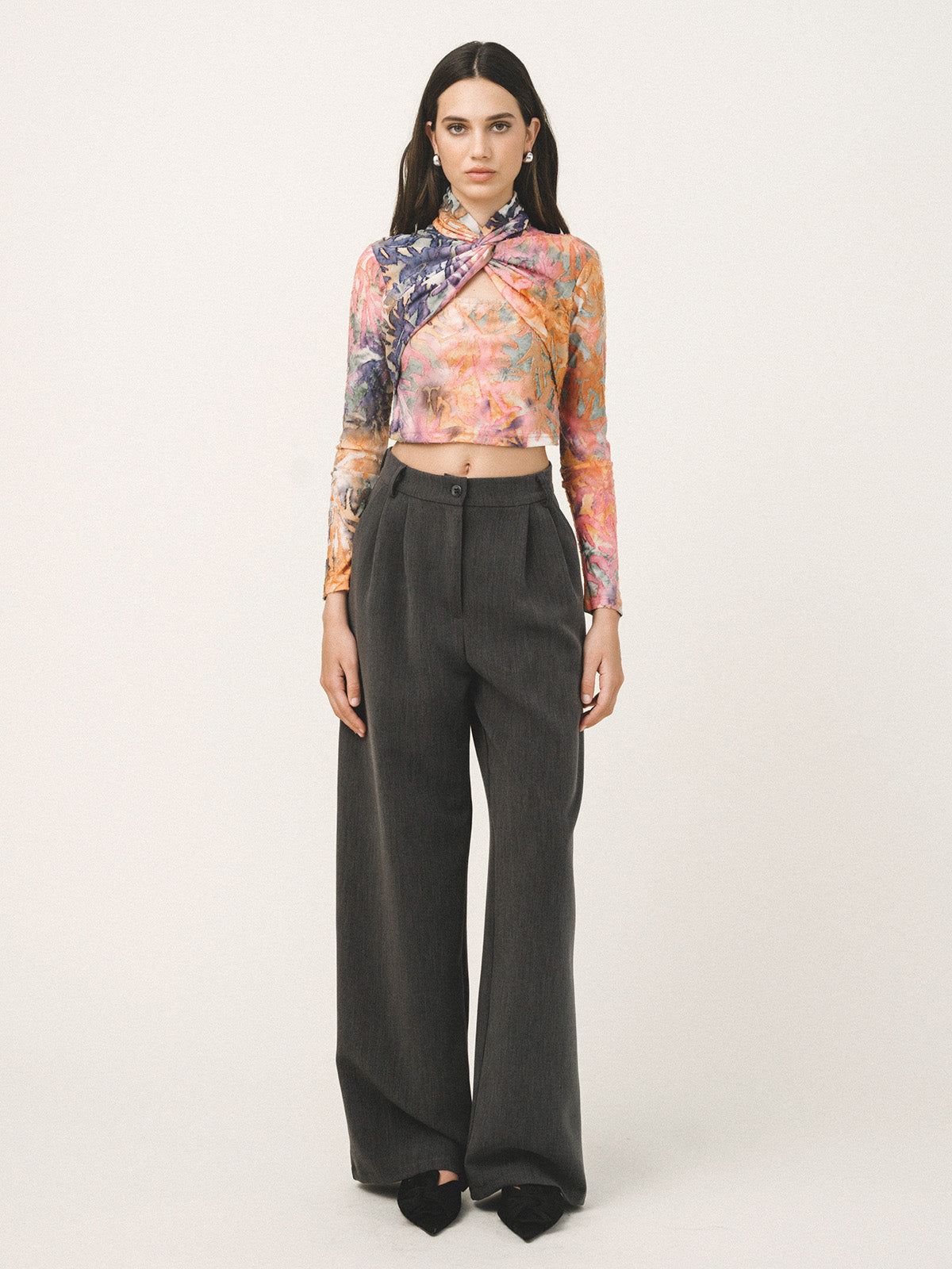 Woman wearing a colorful floral top and black high-waisted pants on a white background