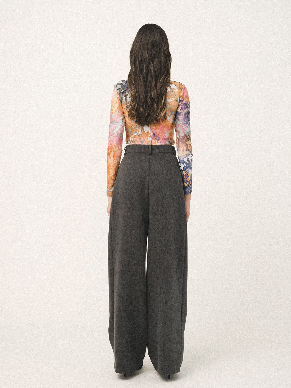 Person wearing a colorful floral top and dark gray wide-leg pants on a white background