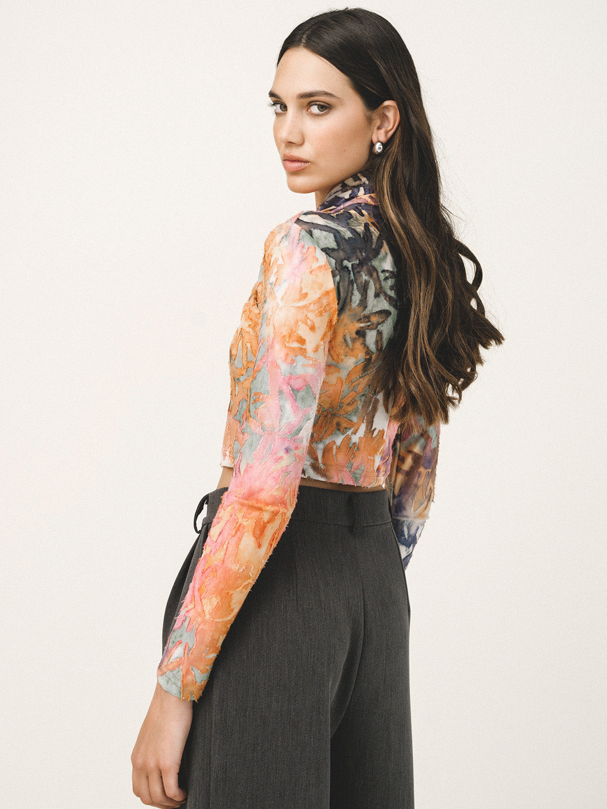 Woman wearing a colorful floral blouse with long sleeves on a plain background