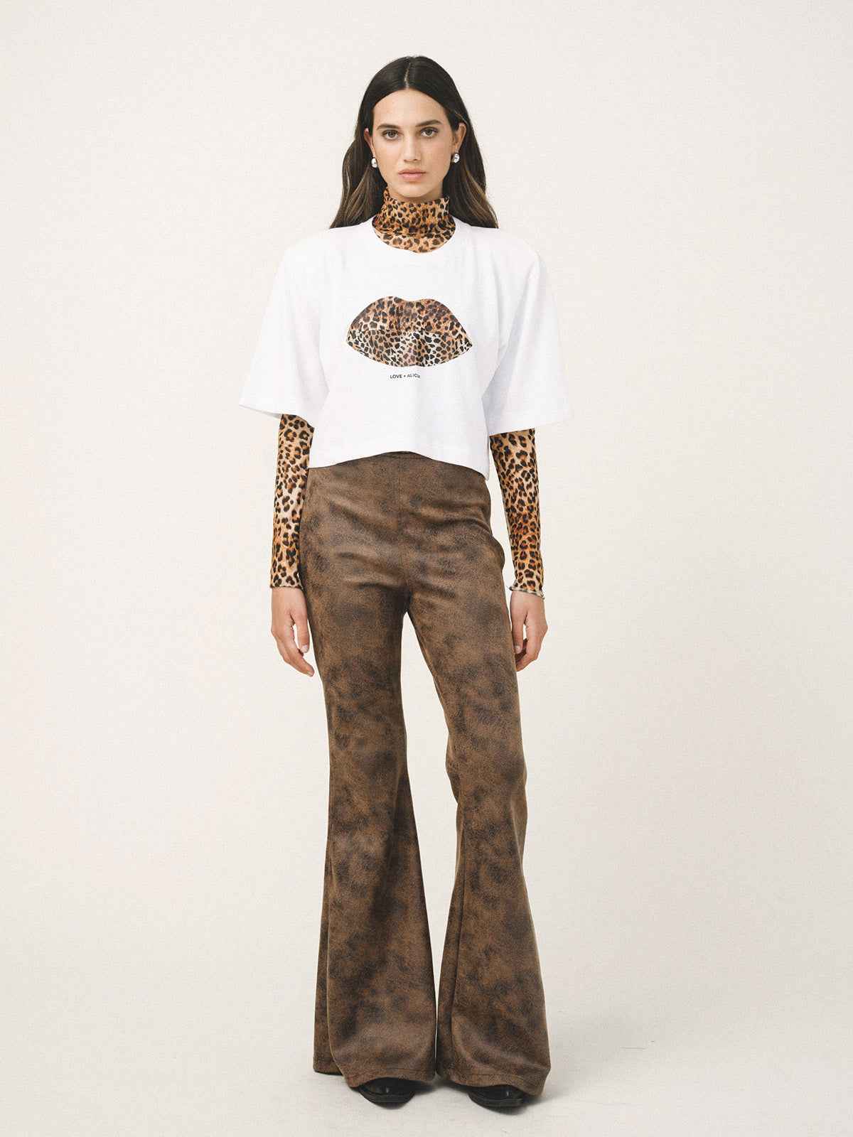 Model wearing a white t-shirt with a leopard print design and brown flared pants on a white background