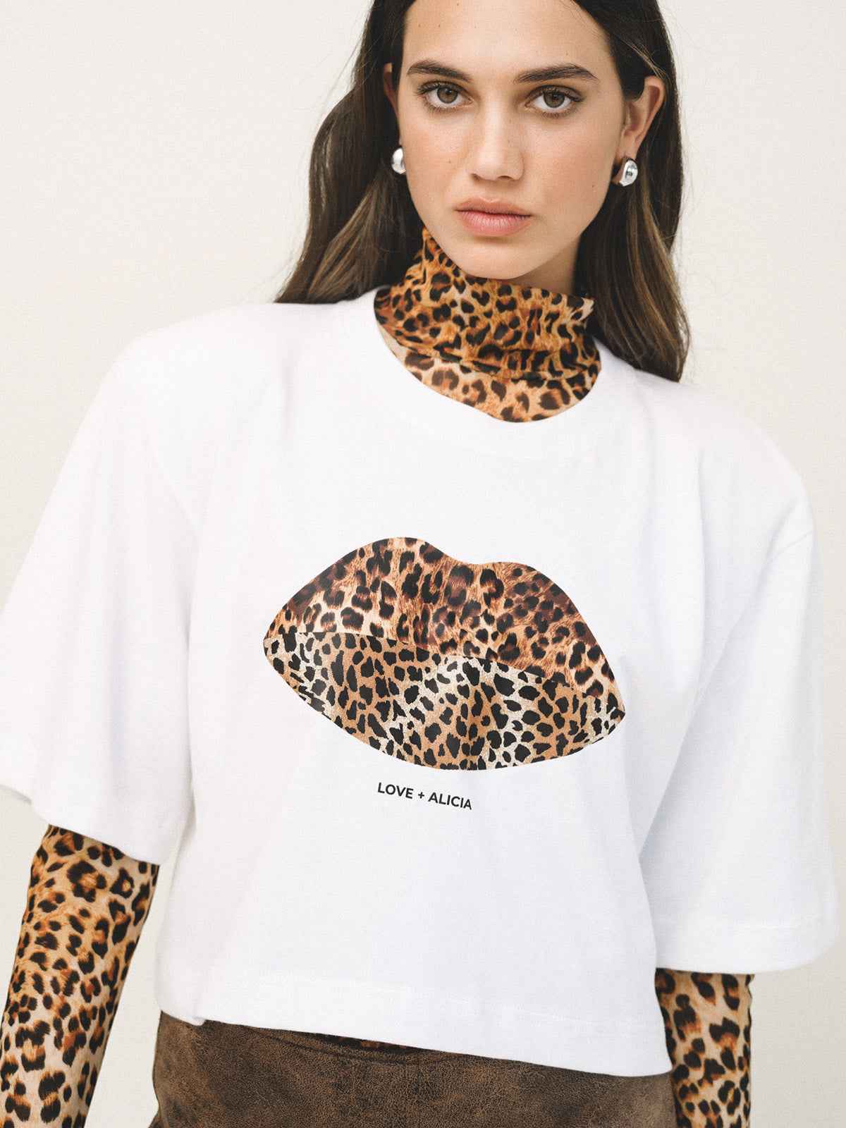 Woman wearing a white t-shirt with leopard print lips design and text, standing against a plain background.