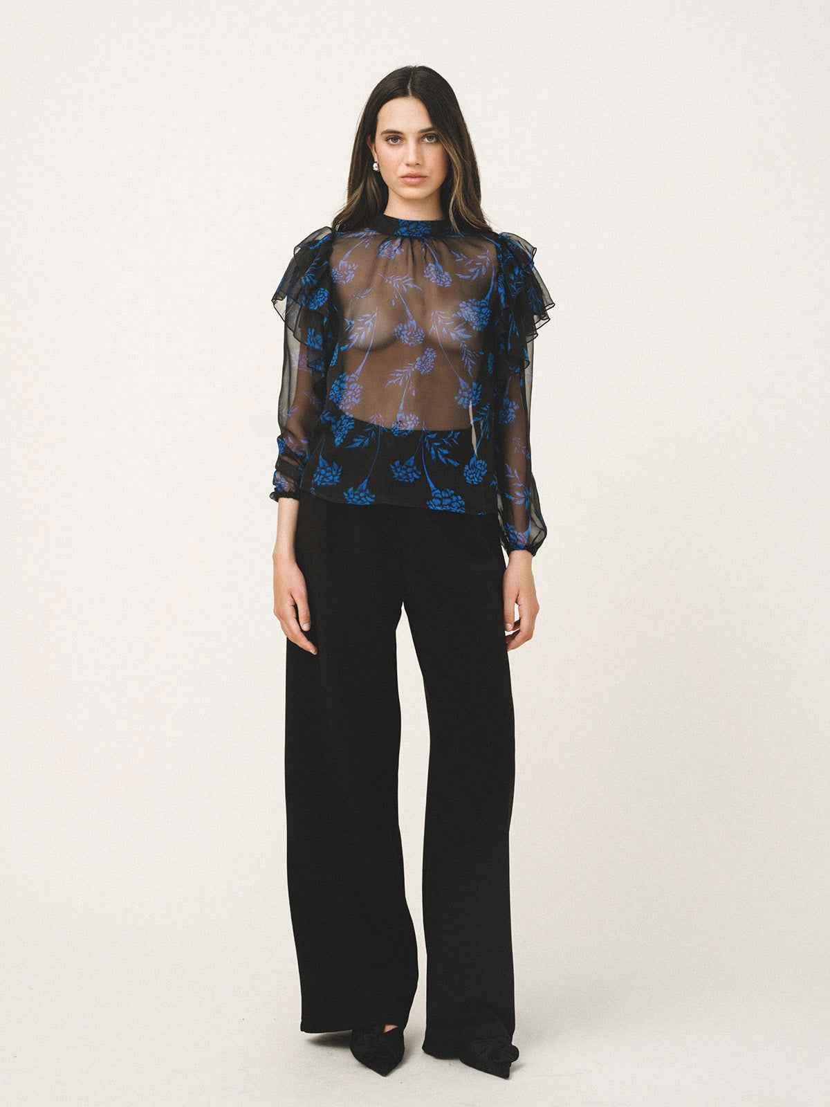 Woman wearing a sheer blue floral blouse with black pants on a white background