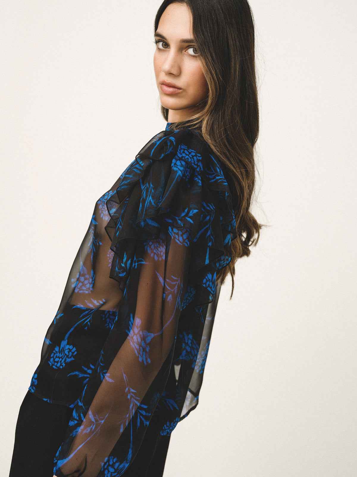 Woman wearing a black sheer top with blue floral patterns on a white background