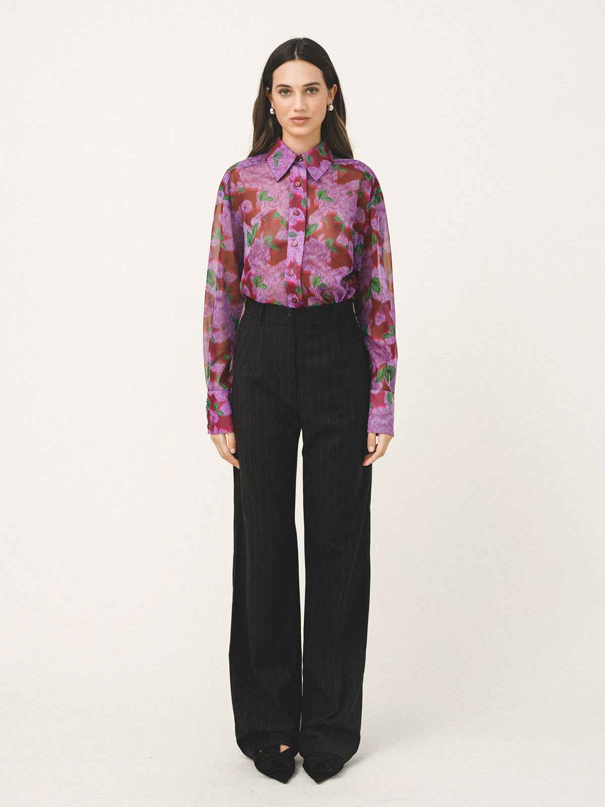 Woman wearing a floral blouse and black pants on a white background