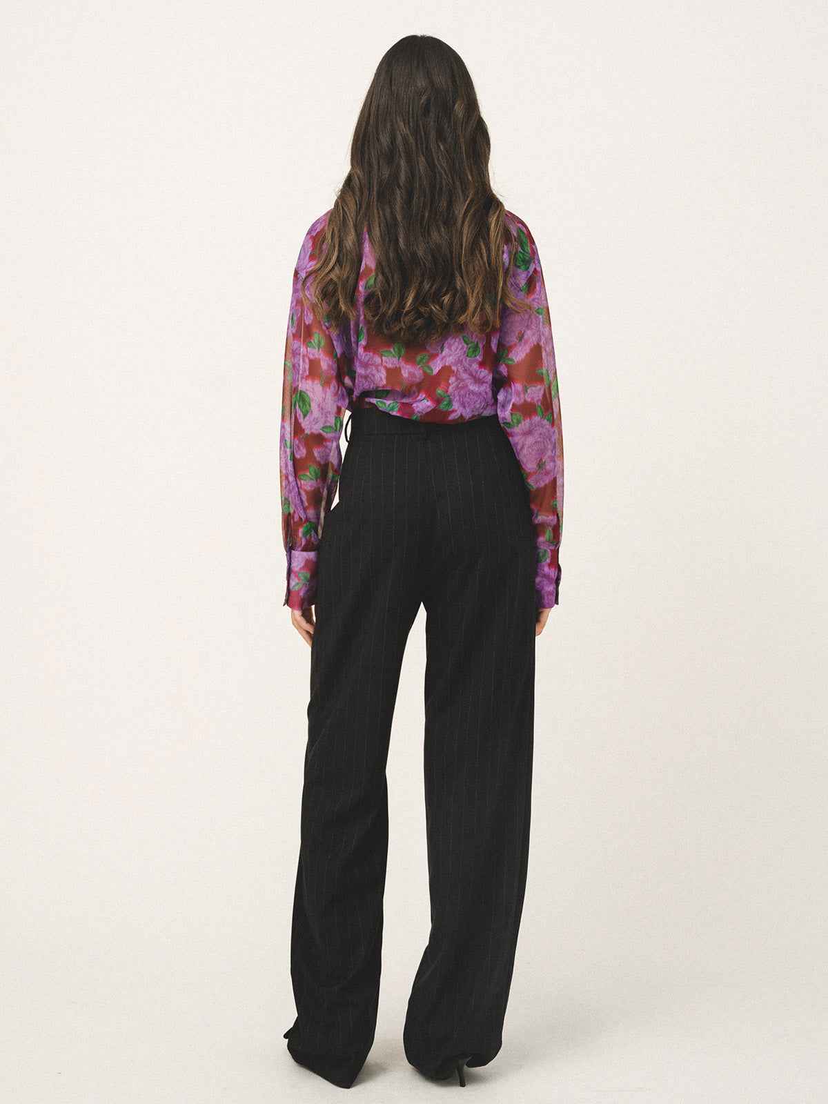 Person wearing a colorful floral blouse and black pants on a white background
