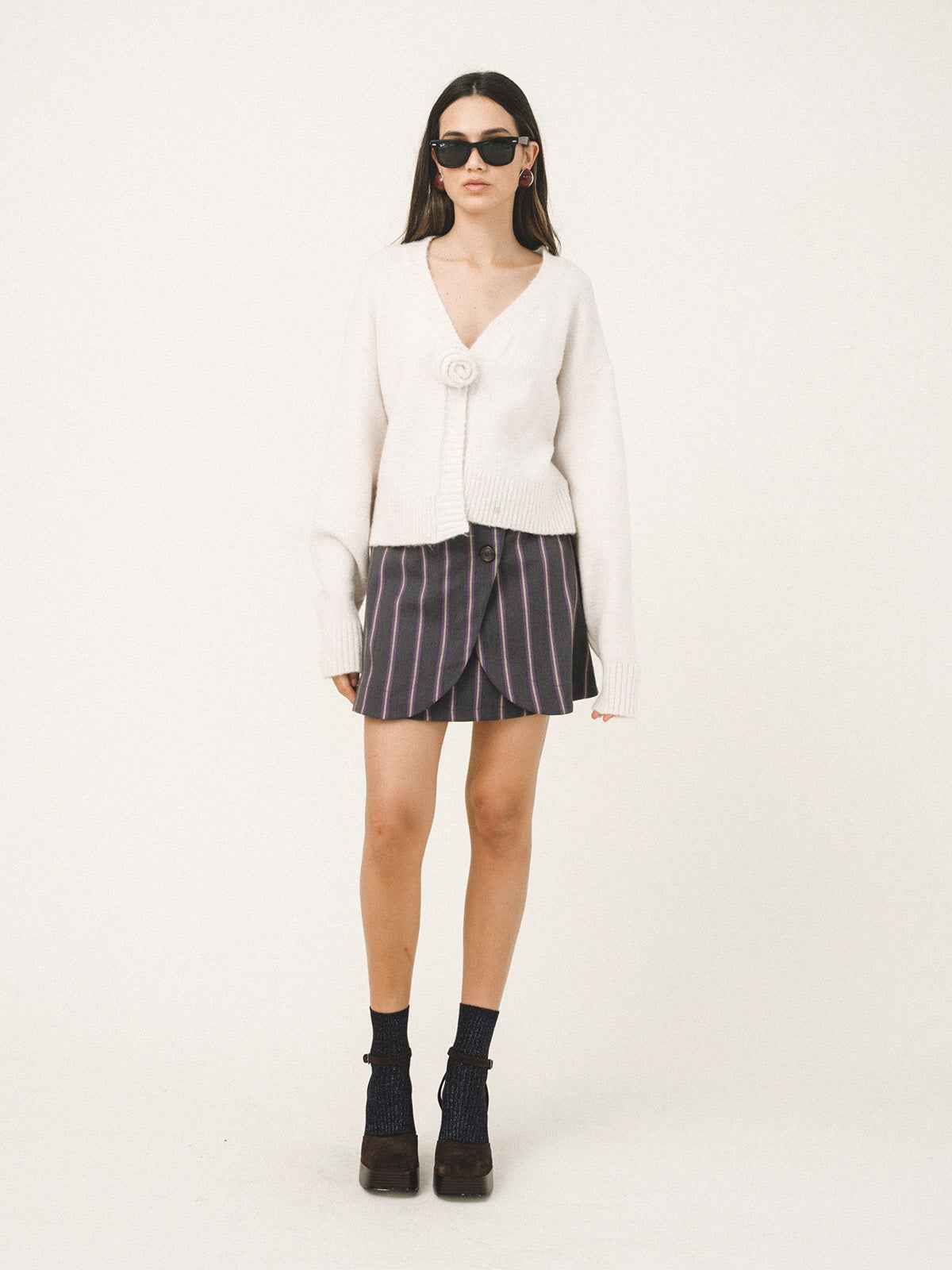 Woman wearing a white cardigan, striped skirt, and black boots on a white background
