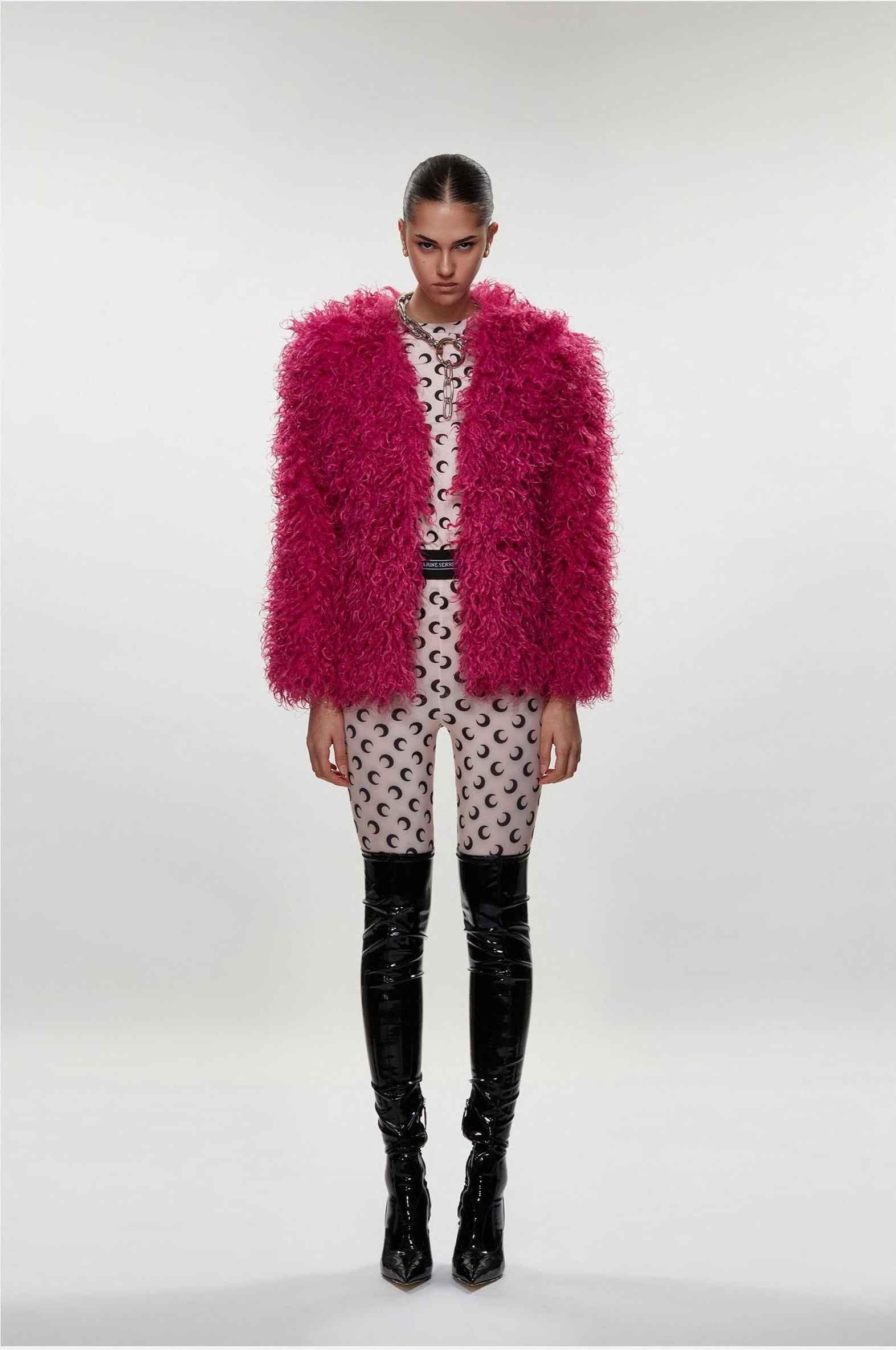 Model wearing a bright pink fluffy coat over a patterned outfit on a white background