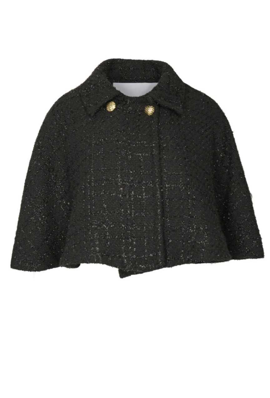 A model wearing a black tweed cape with gold button details and a flared silhouette, paired with a matching skirt.