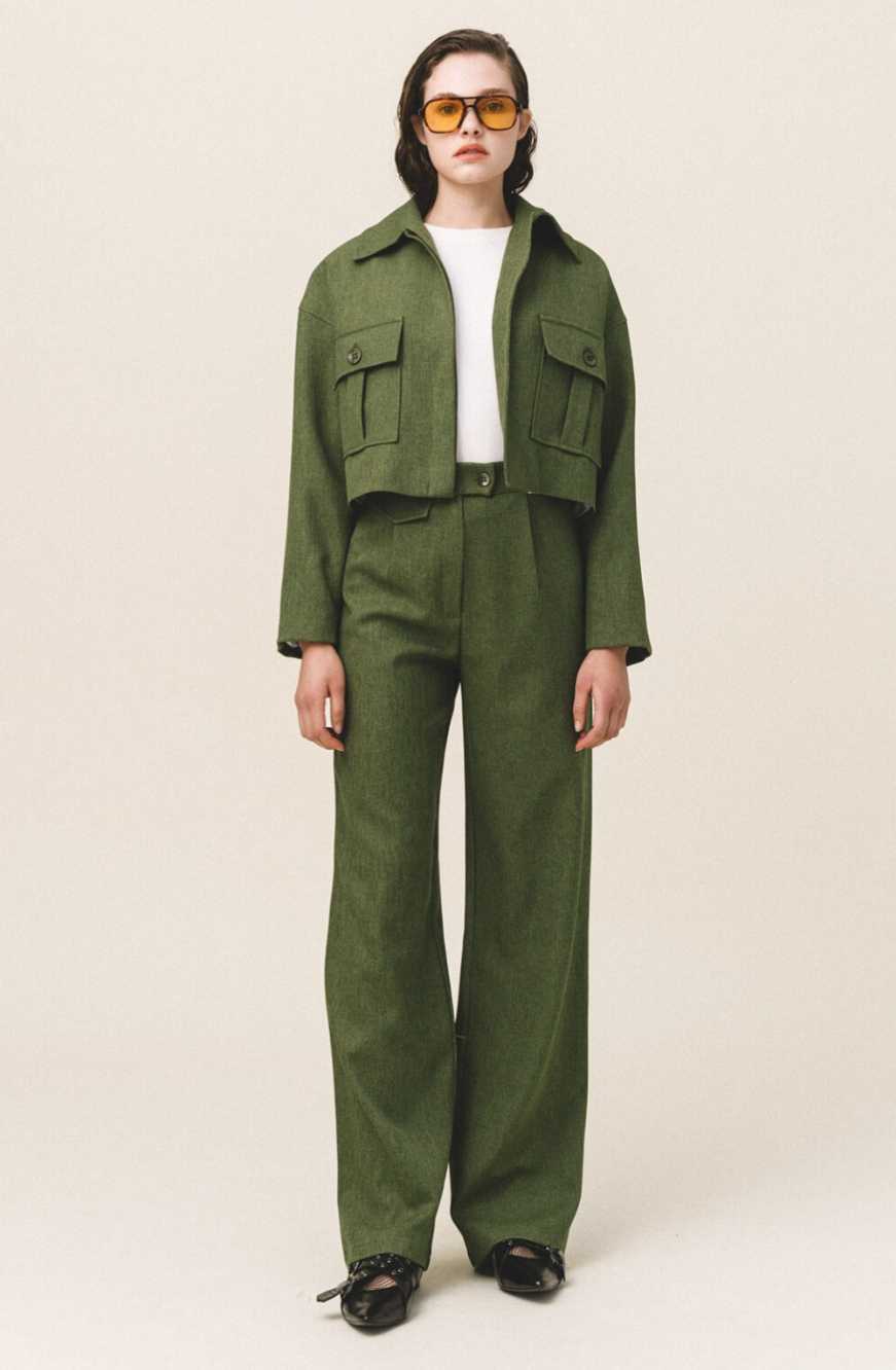 A woman wearing a green button-up crop jacket with large flap pockets and a white top.