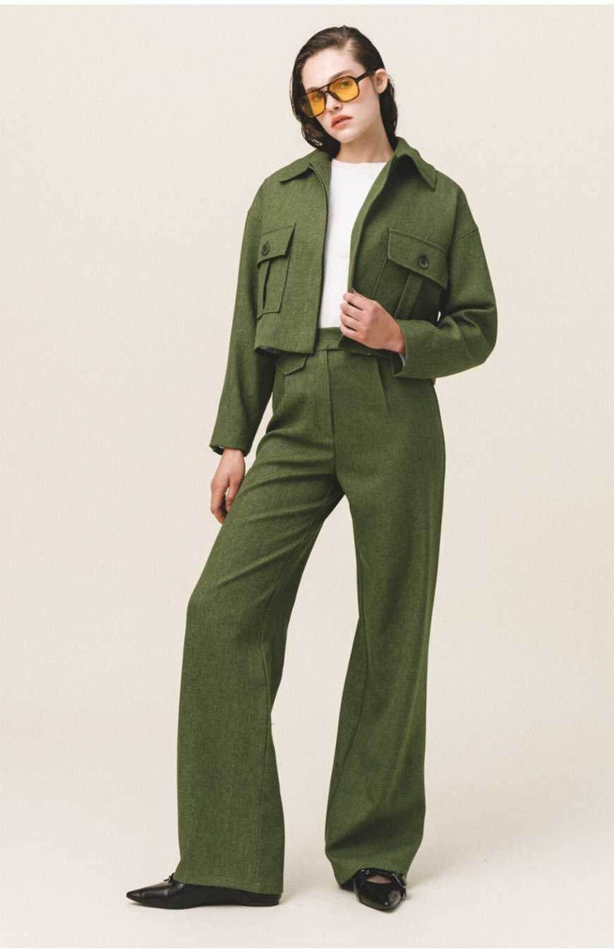 A woman wearing a green button-up crop jacket with large flap pockets and a white top.