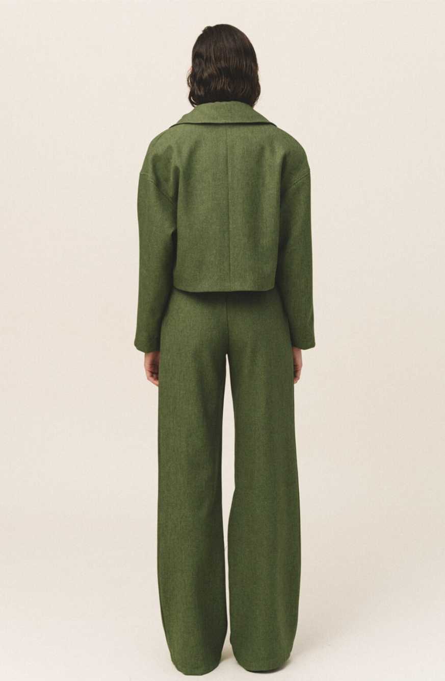 A woman wearing a green button-up crop jacket with large flap pockets and a white top.