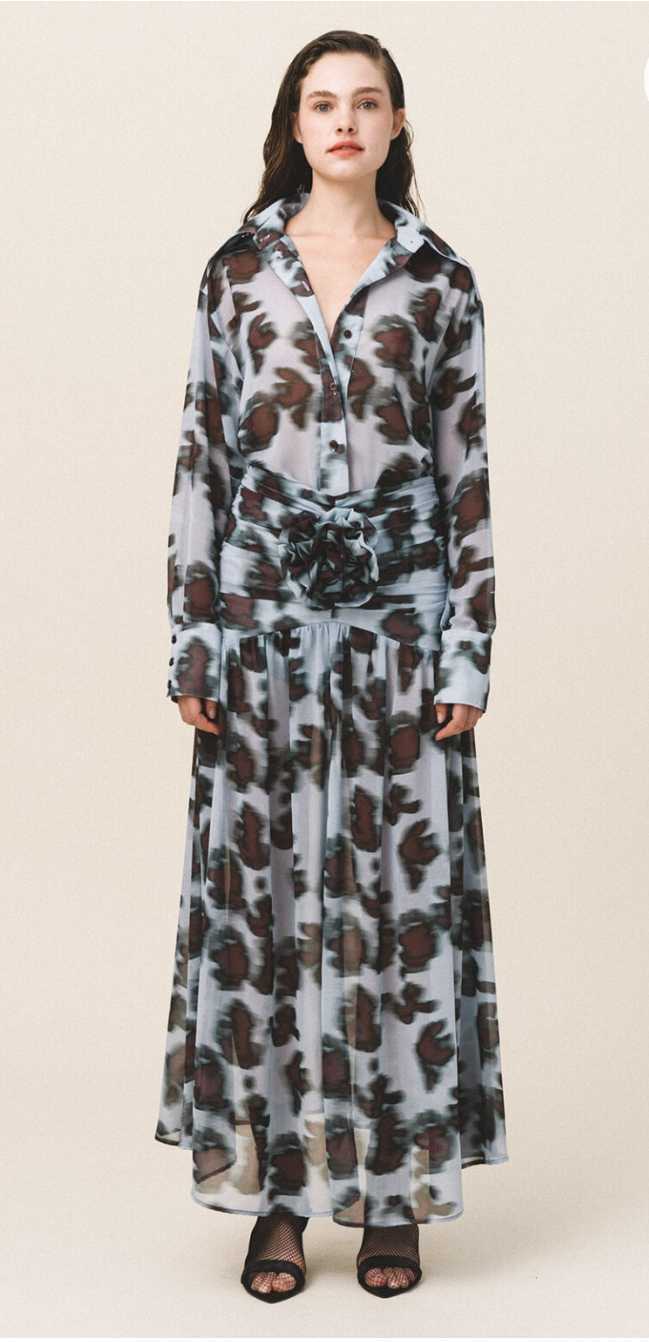 A model wearing an oversized sheer shirt with a geometric animal pattern, featuring a loose fit and buttoned cuffs, paired with a matching long skirt.
