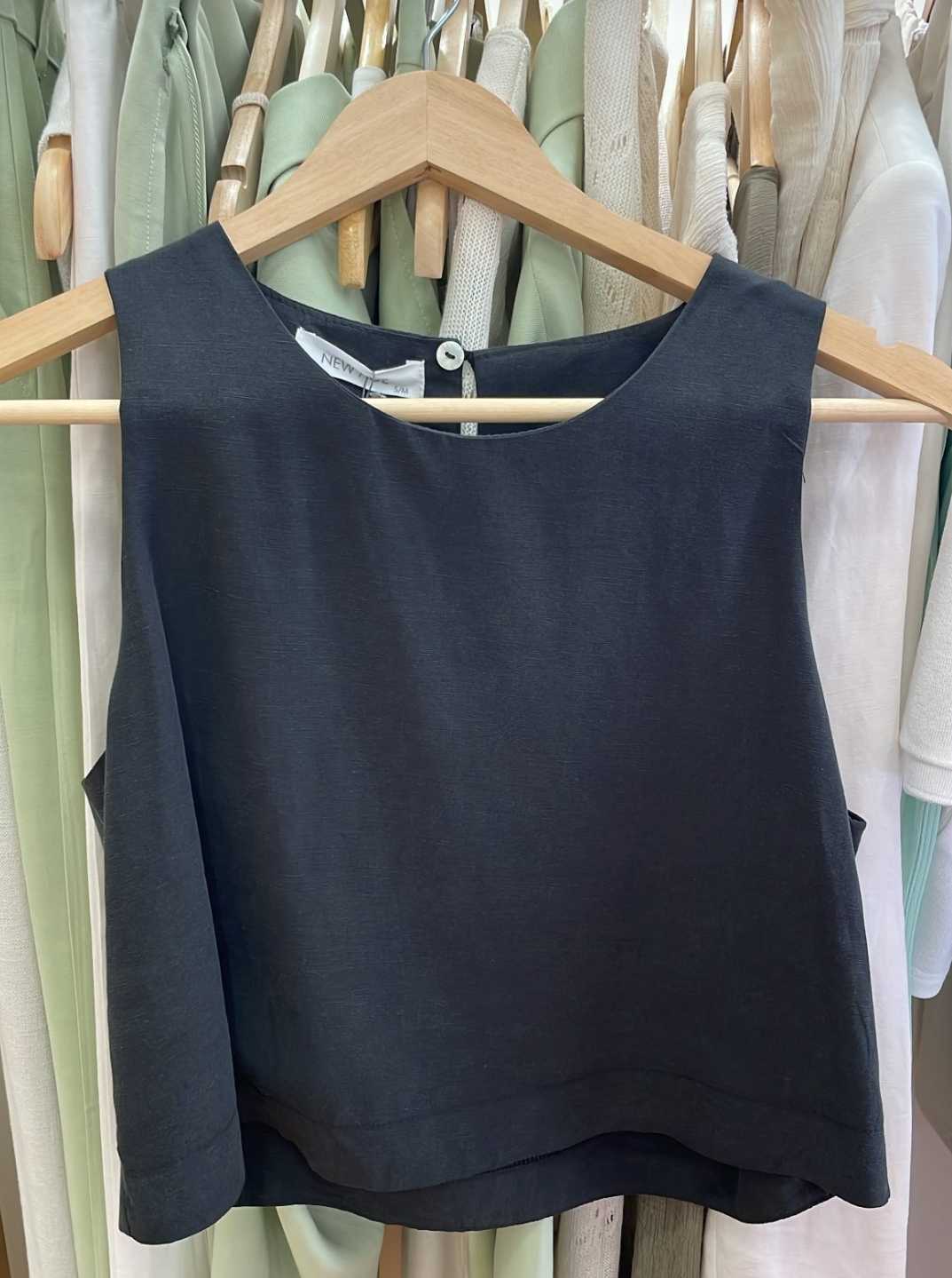 Black sleeveless top on a wooden hanger against a background of other clothing.