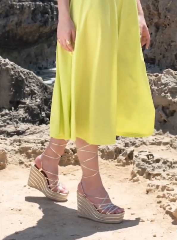 Person wearing a bright yellow dress and pink sandals with white straps on a rocky beach.