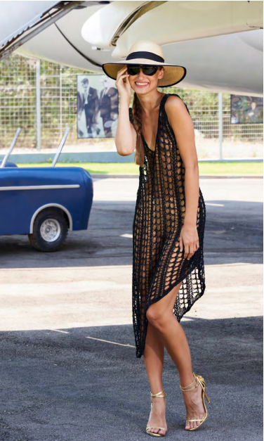 Woman in a black crocheted dress and hat standing next to a vintage car.