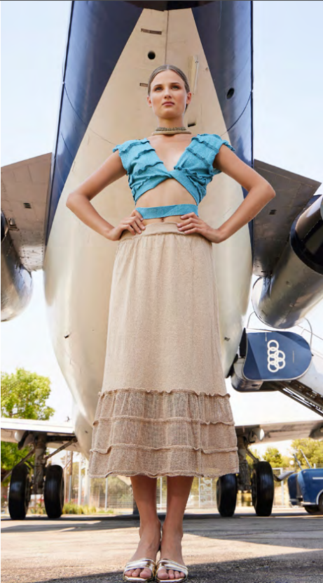 Woman in a blue top and beige skirt standing in front of an airplane